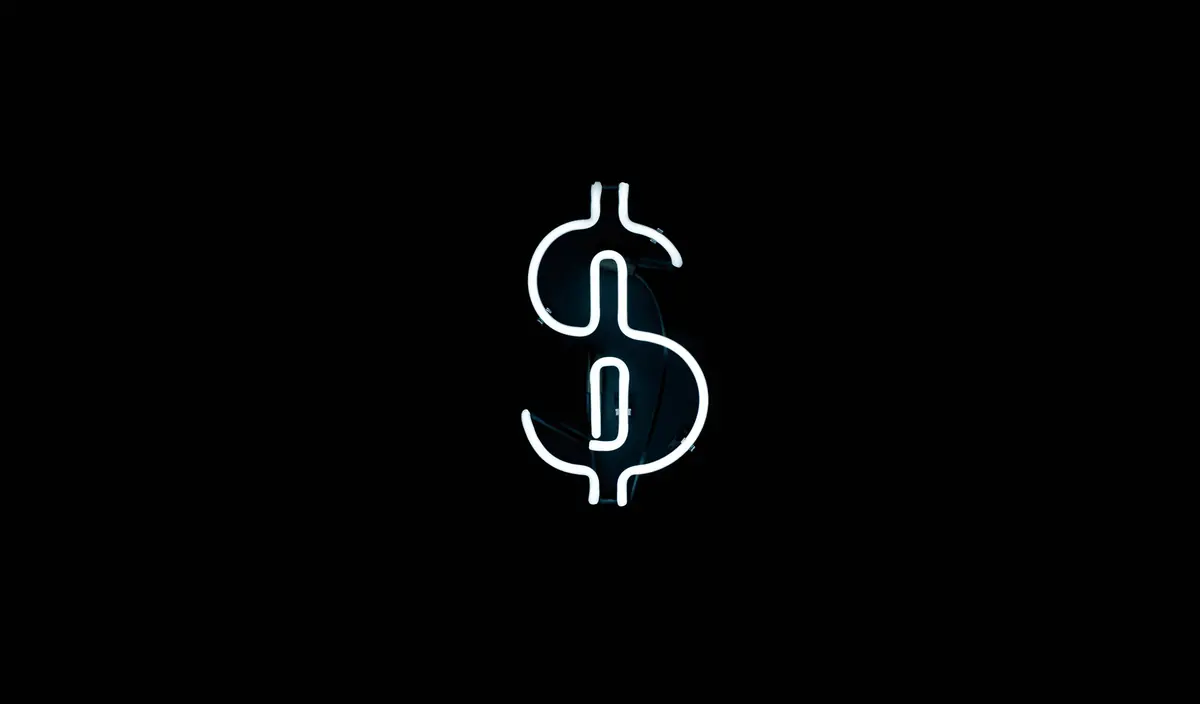 A neon dollar sign glowing on a black wall
