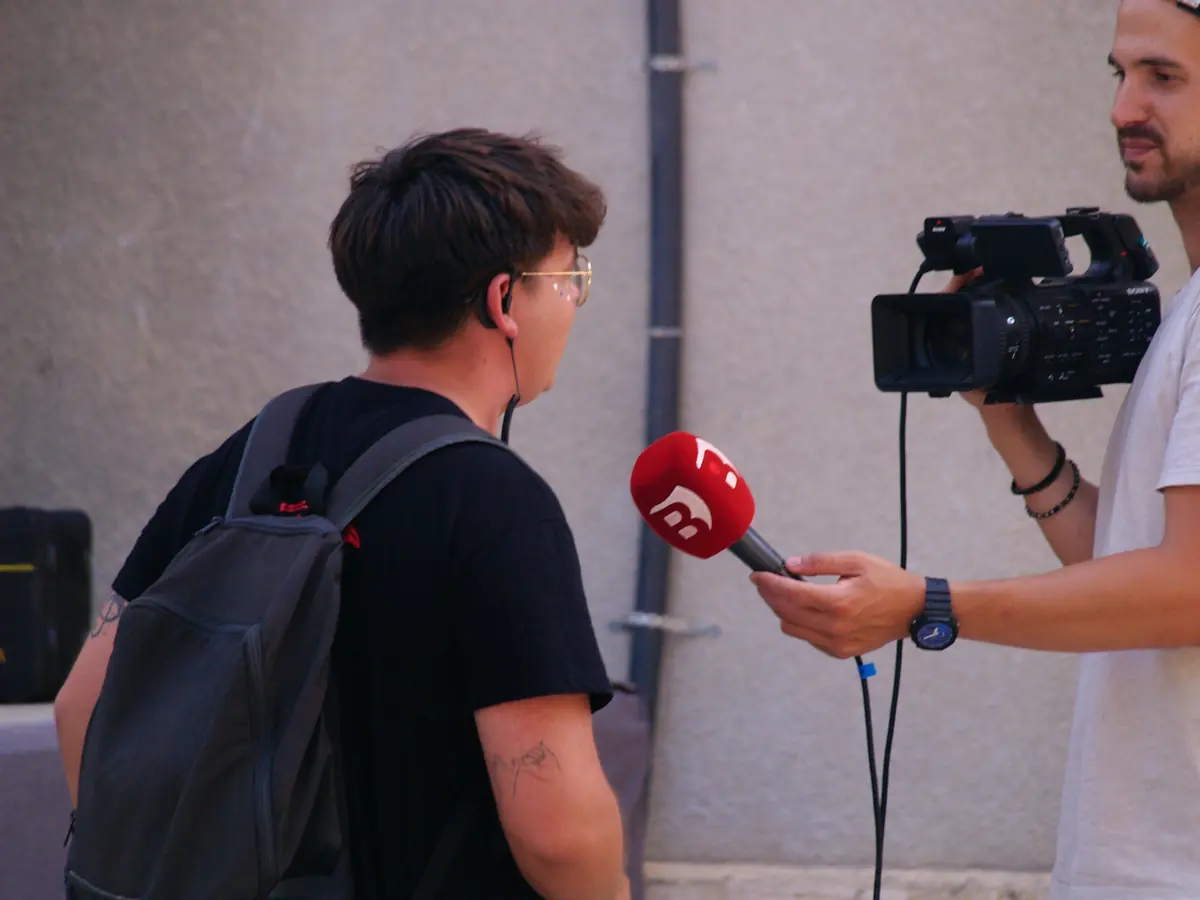 A reporter holding a microphone while a camera operator films a street interview